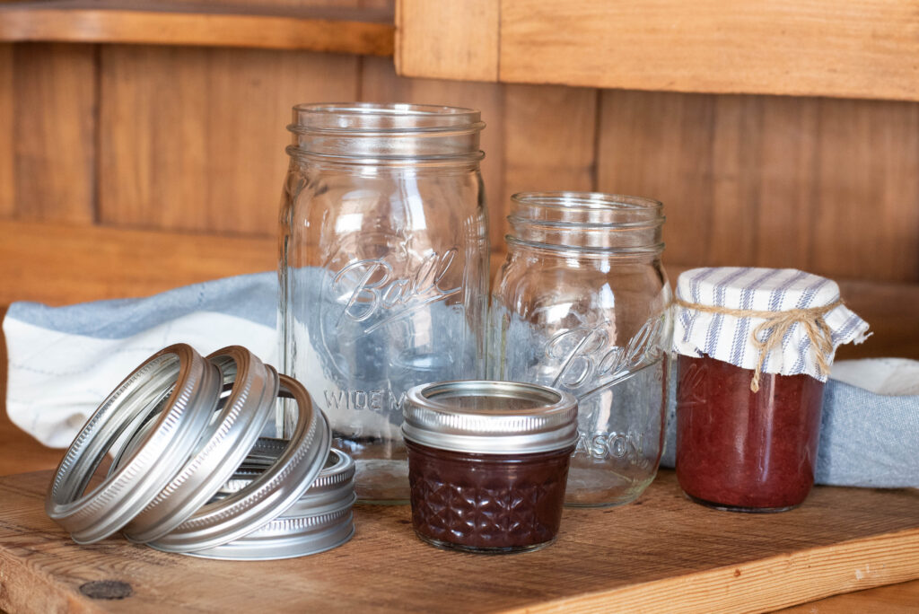 Ball Mason jars and lids and jars of jam arranged on wood cutting board