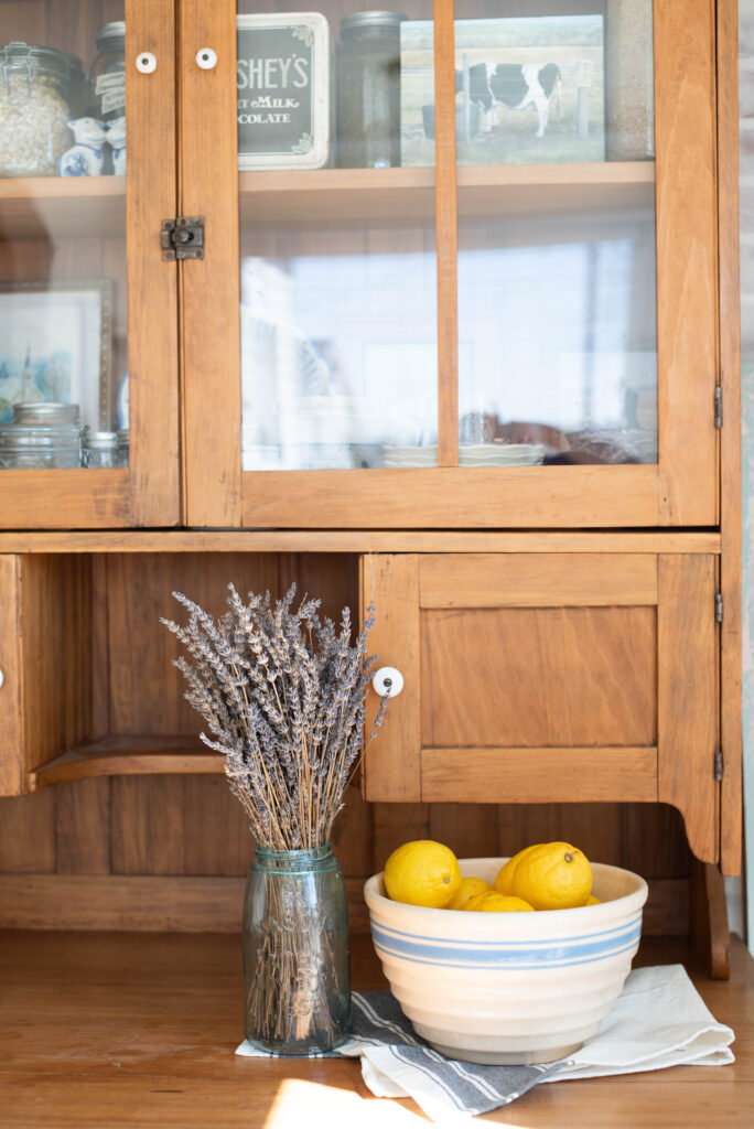 Bowl of lemons in antique stoneware next to antique jar of dried lavender displayed on bakers hutch