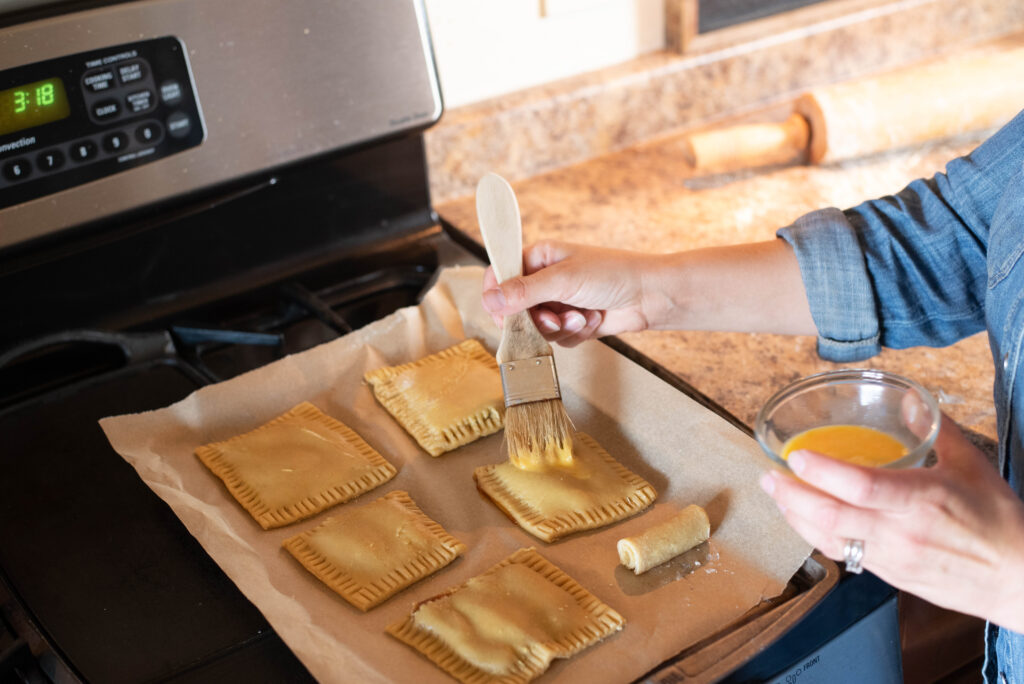 Egg wash being brushed onto hand pies before baking