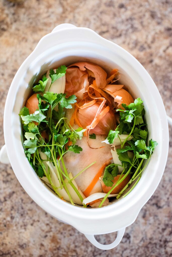 Whole chicken in a slow cooker with fresh parsley and veggie scraps