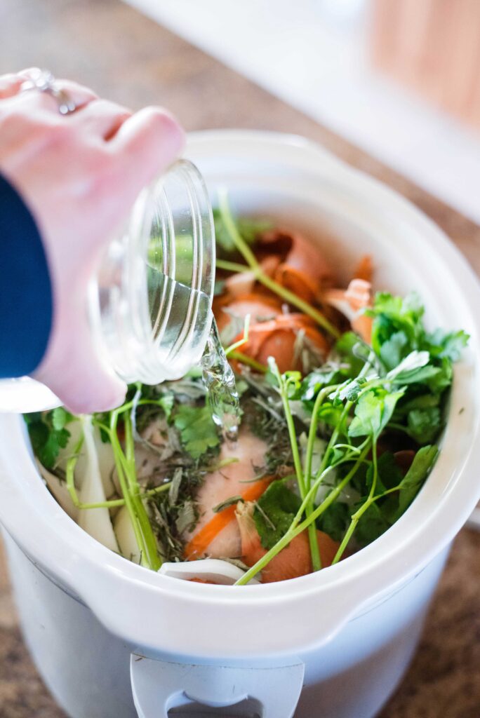 Water being added to slow cooker with veggie scraps and chicken