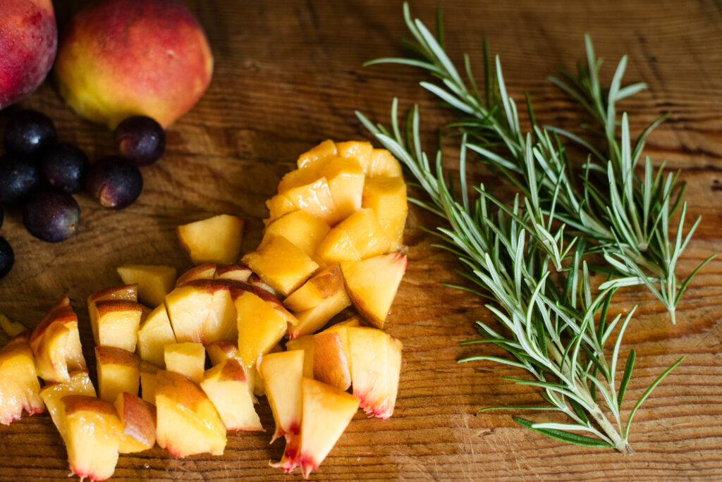 Peaches, grapes and rosemary resting on cutting board
