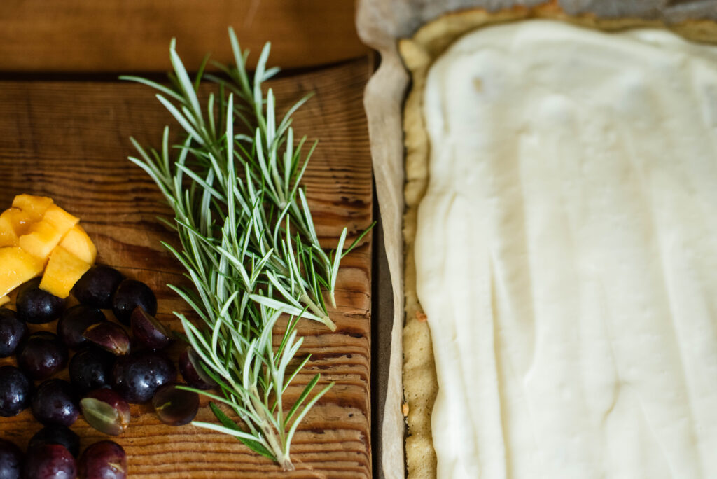 Ganache spread over sugar cookie crust with rosemary, grapes and peaches for fruit pizza