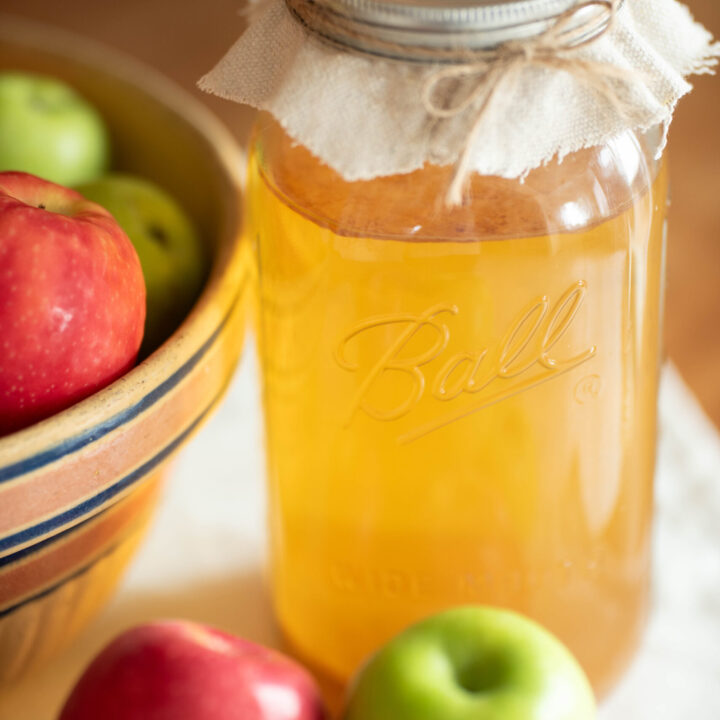 Jar of homemade apple cider vinegar surrounded by fresh apples.