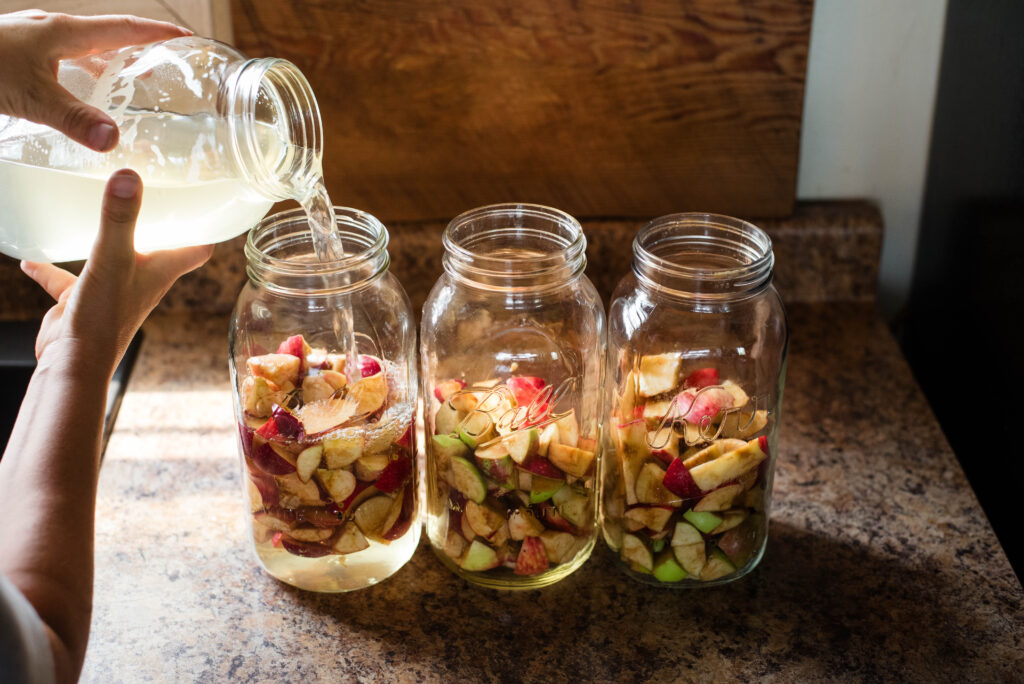 Sugar water being poured over apple scraps for homemade apple cider vinegar.