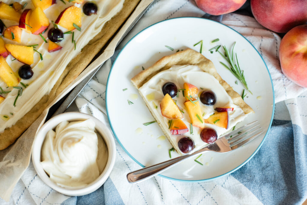 Fruit pizza with peaches and grapes and bowl of whipped vanilla bean ganache