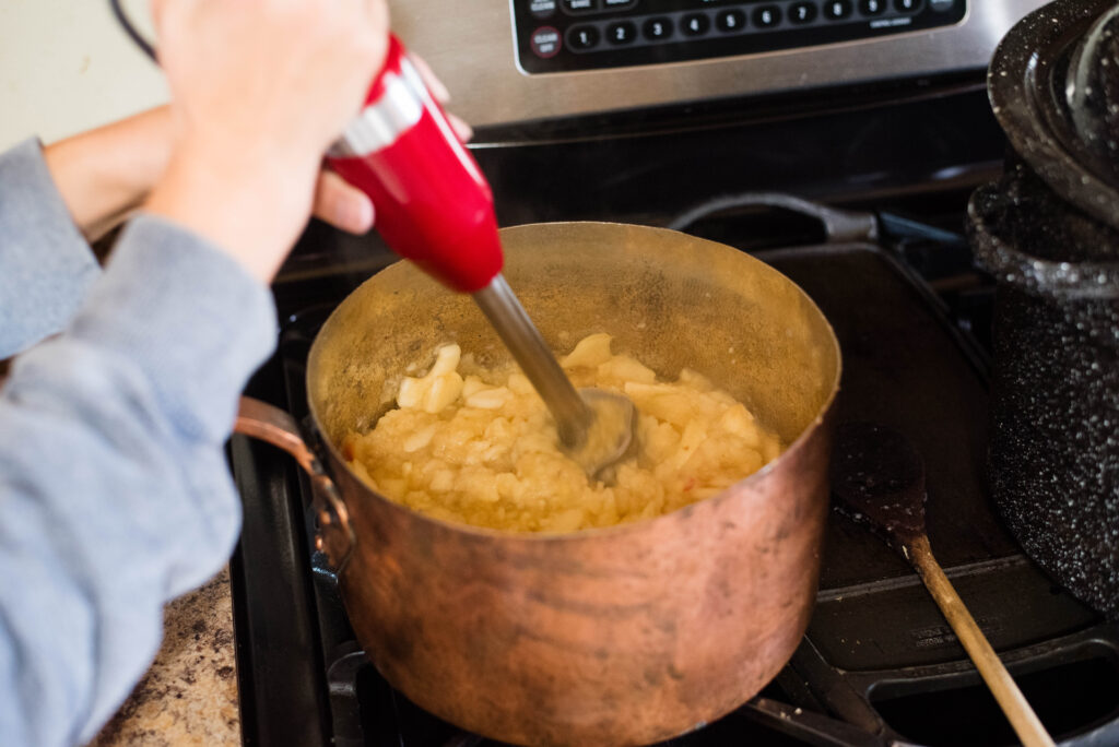 Cooked apples being pureed with immersion blender.