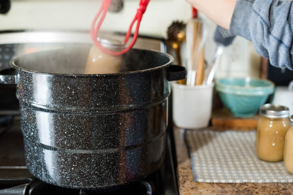 Jars of applesauce being pulled out of water bath canner.