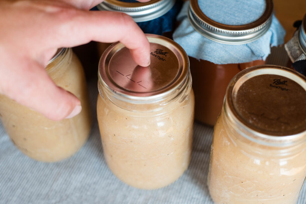 Finger testing the seal on a canned jar of applesauce.