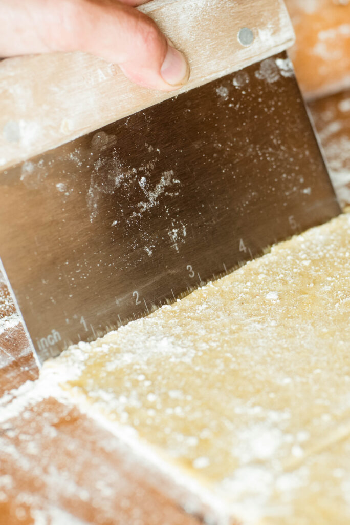 Bench scraper measuring length of dough for hand pies.