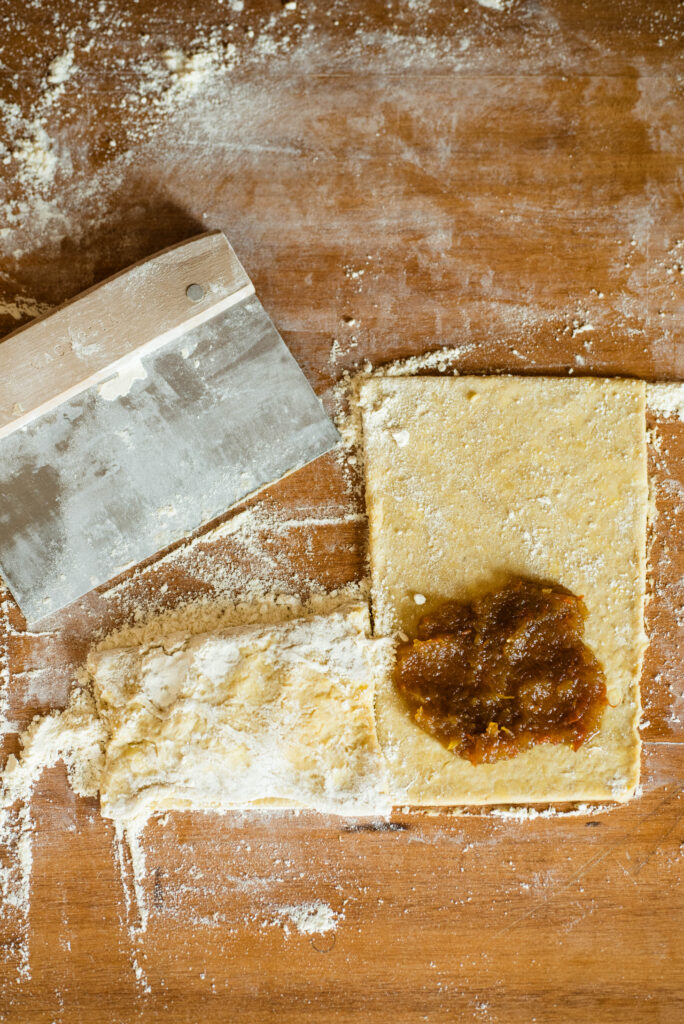 Pumpkin filling scooped onto strip of pie dough for pumpkin hand pies.