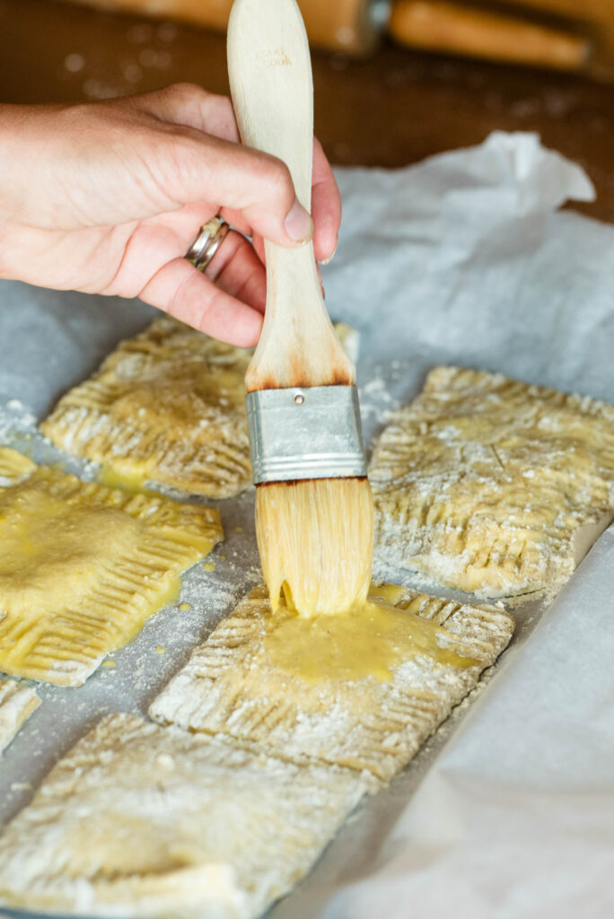 Egg wash being brushed onto hand pies before baking.