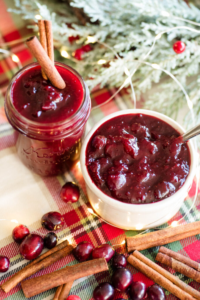 Spiced cranberry Christmas jam in a bowl with cranberries and cinnamon sticks