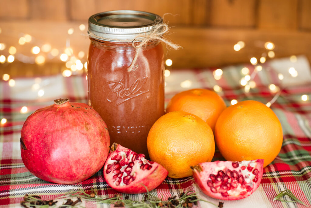 jar of cocktail shrub with pomegranates and oranges