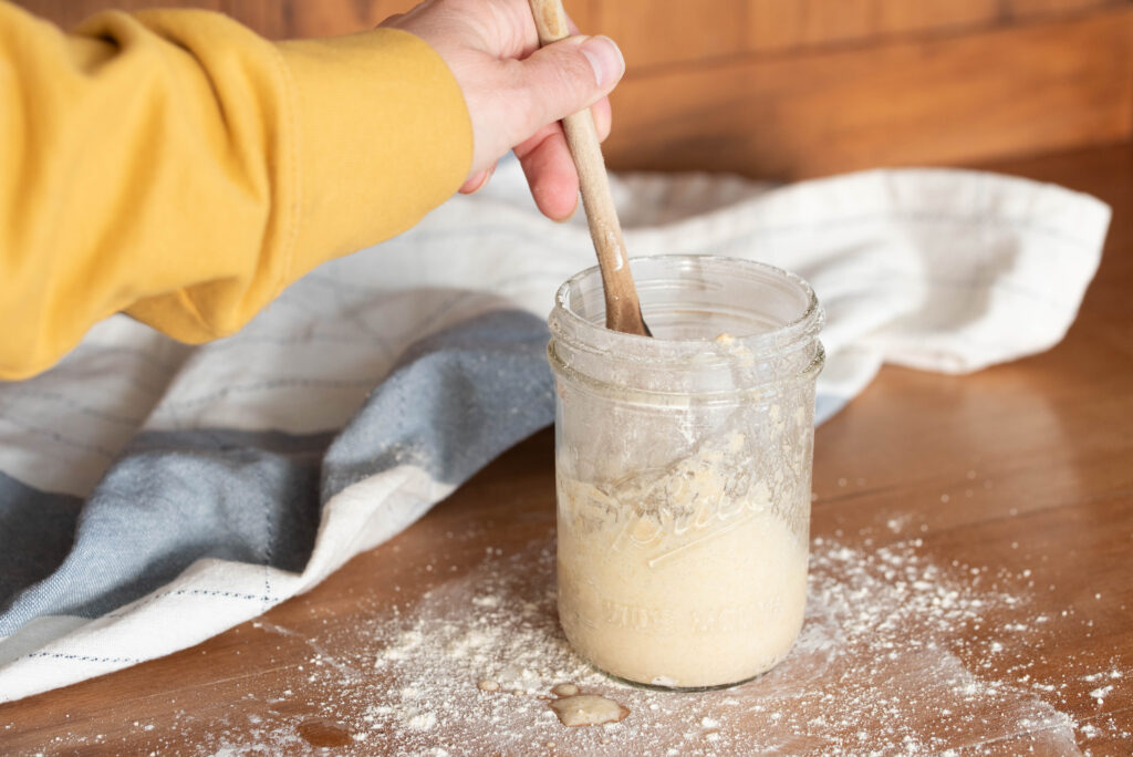 sourdough starter being stirred with a wooden spoon