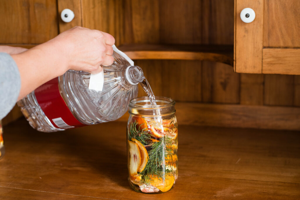 Vinegar being poured onto orange peels and pine branches for an all-natural all-purpose cleaner