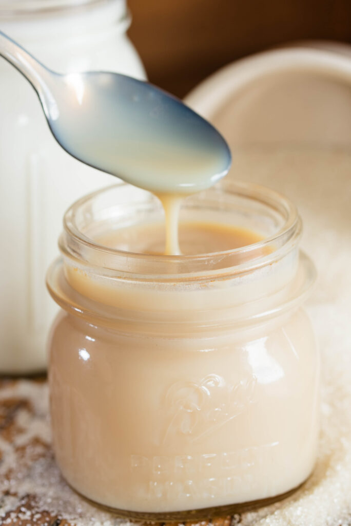 Homemade sweetened condensed milk drizzling from a spoon