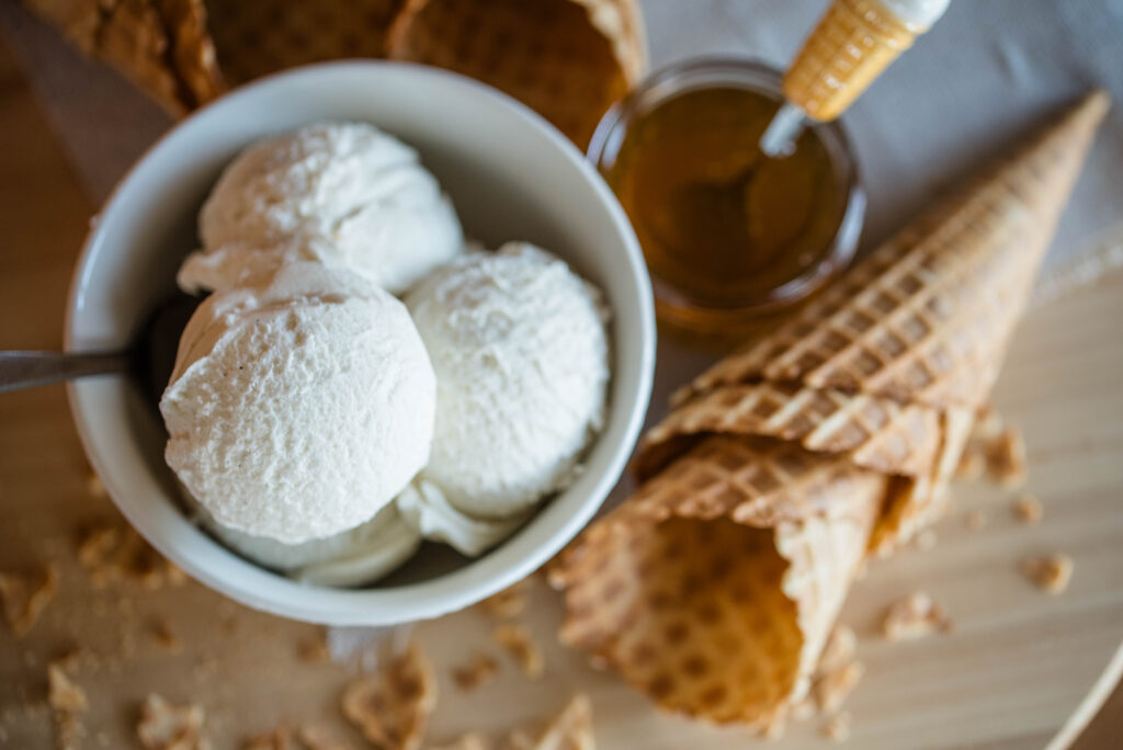 Bowl of homemade vanilla ice cream with jar of honey and waffle cones.