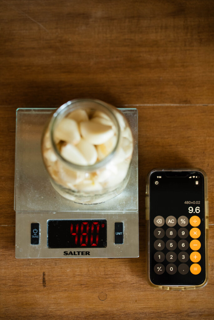 Jar of fresh garlic cloves on a digital scale with a calculator.
