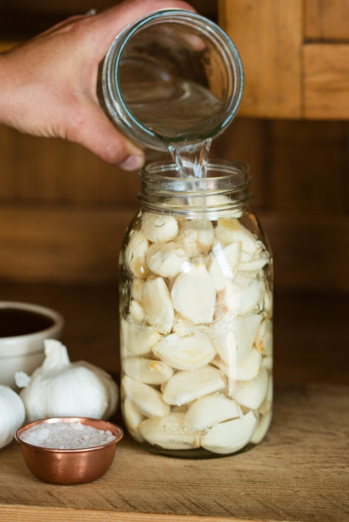 Saltwater brine being poured over fresh garlic cloves for fermenting.