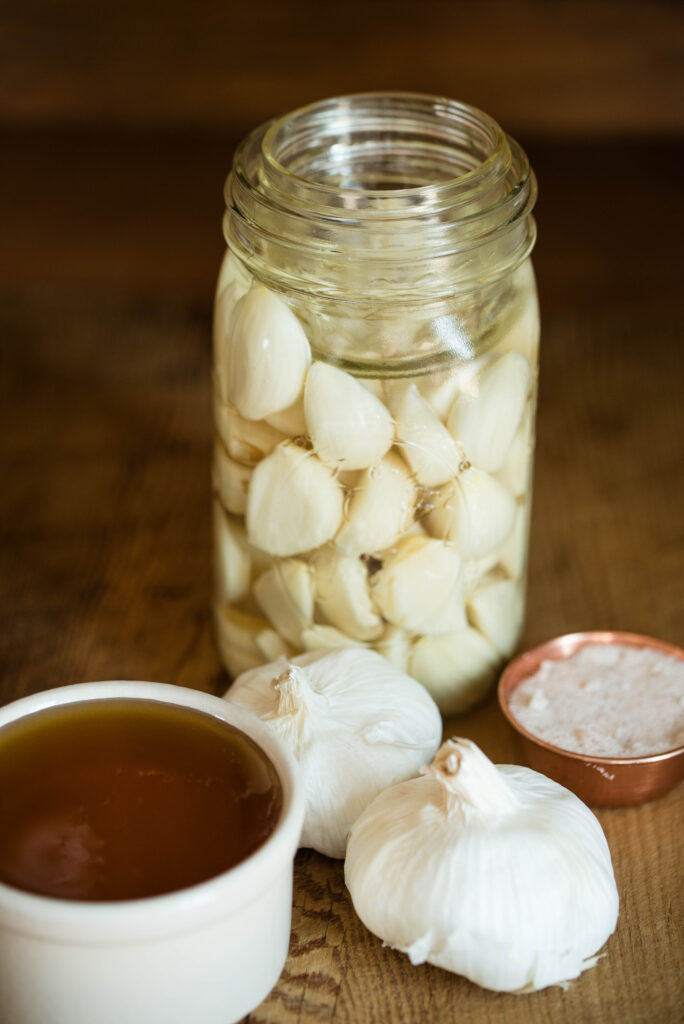 Jar of fermented garlic with a quarter pint size jar submerging garlic below the brine.