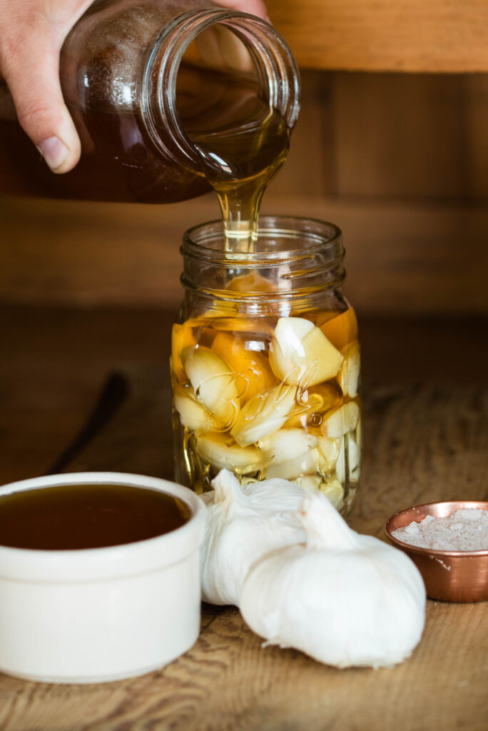 Honey being poured over fresh garlic cloves for fermenting.