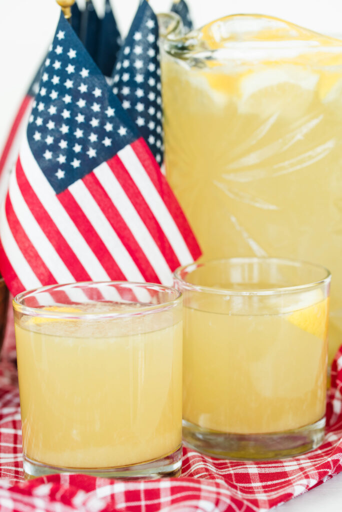 Two glasses of lemonade with a pitcher of lemonade and American flag in the background.