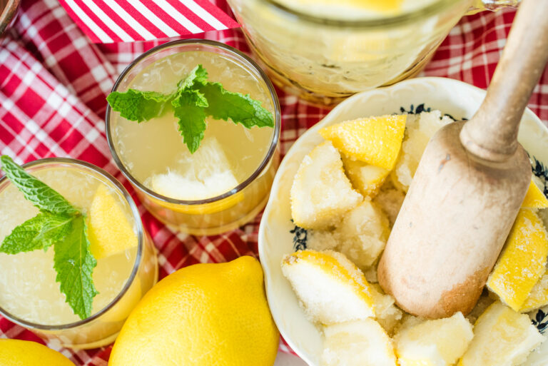 Two glasses of homemade lemonade with bowl of lemon slices muddled with sugar.