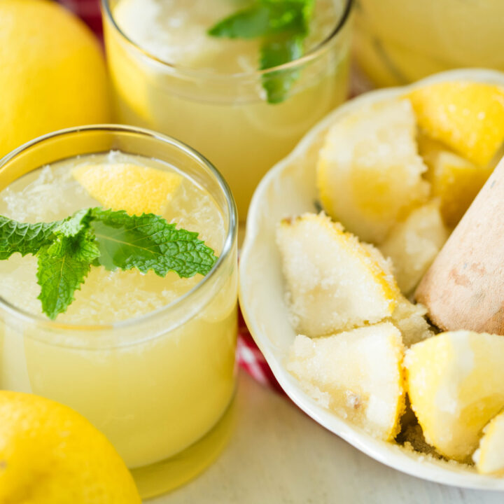 Glass of probiotic old fashioned state fair lemonade with mint and bowl of lemon wedges muddled with sugar.