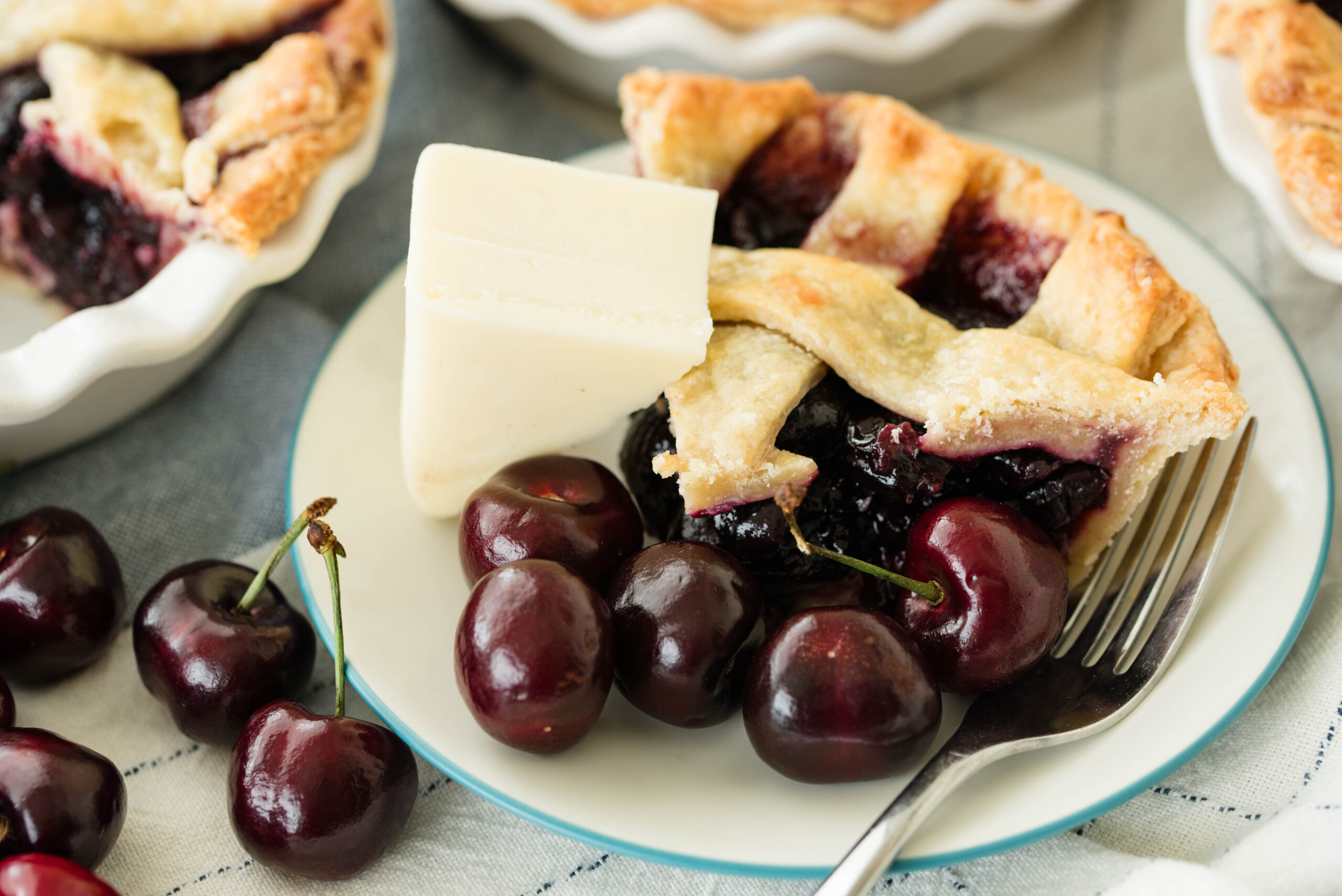 Slice of sourdough door county cherry pie with fresh cherries and wedge of cheese.