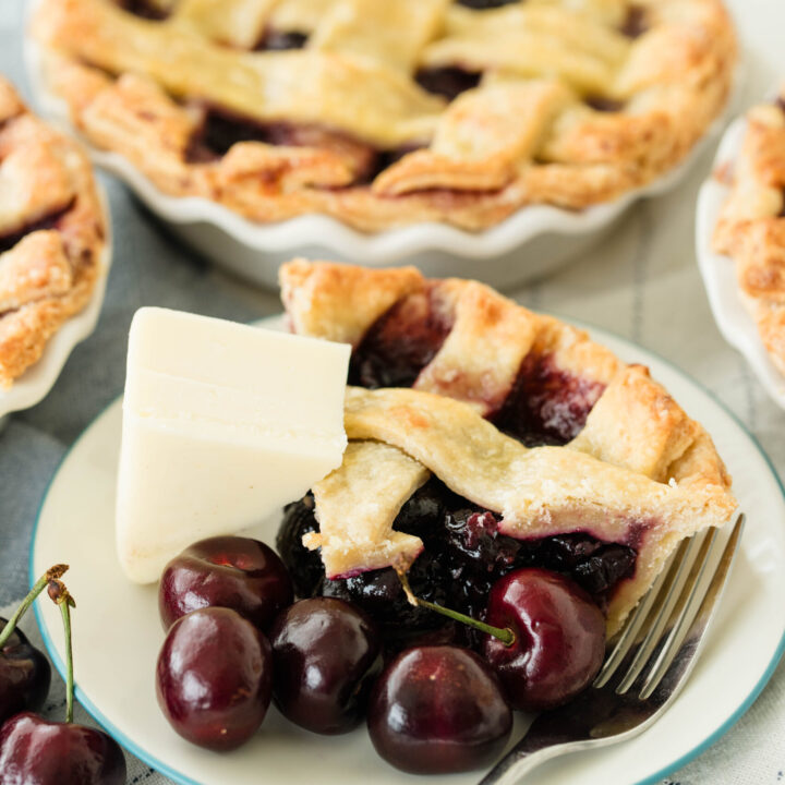 Slice of cherry pie with wedge of cheese and fresh cherries.