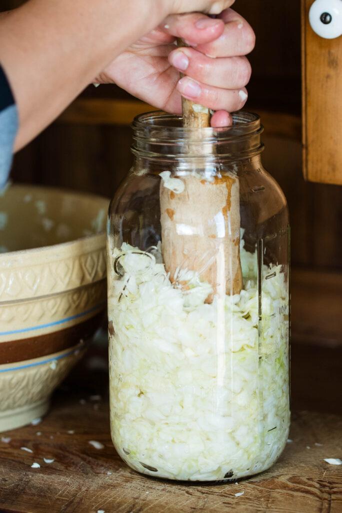 Kraut pounder compacting cabbage in a jar for homemade sauerkraut.