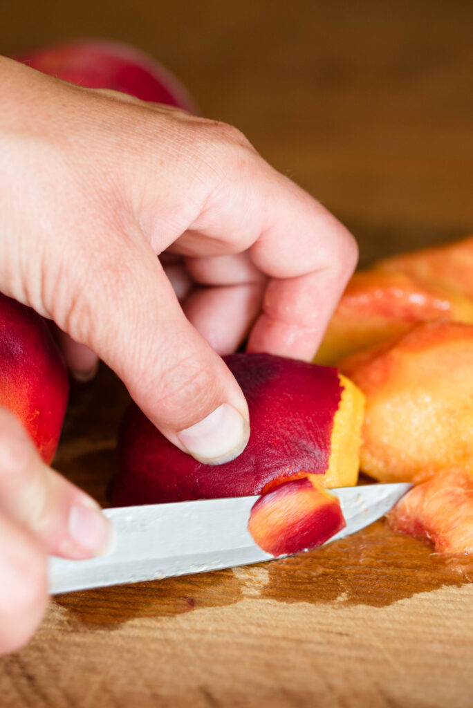 Woman's hand cutting away the skin of peaches.