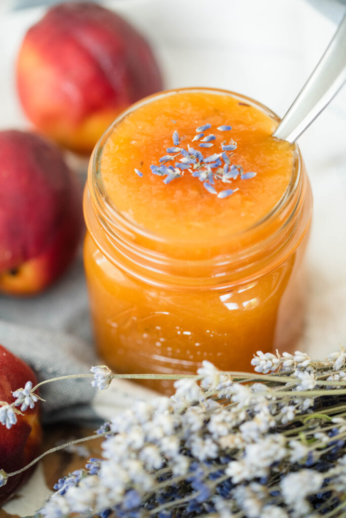 Jar of peach lavender jam with fresh peaches and lavender buds.
