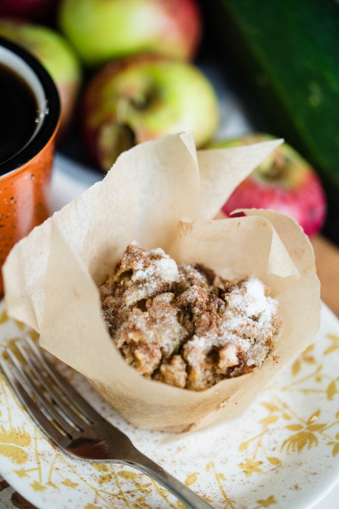 Apple spice muffins on a plate pictured with fresh apples and zucchini.