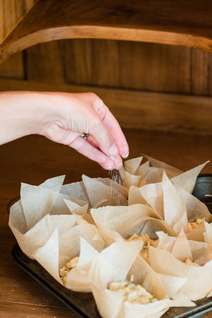 A hand sprinkling sugar on top of apple spice muffins before baking.