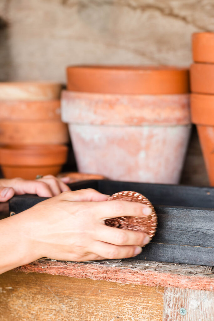 A copper scrubby being used to exfoliate the char off of a wood box.