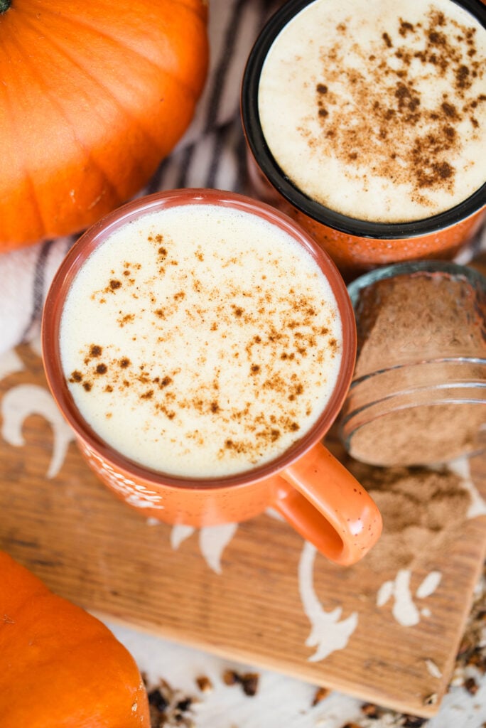 Two mugs of herbal pumpkin spice latte pictured with whole pie pumpkins.