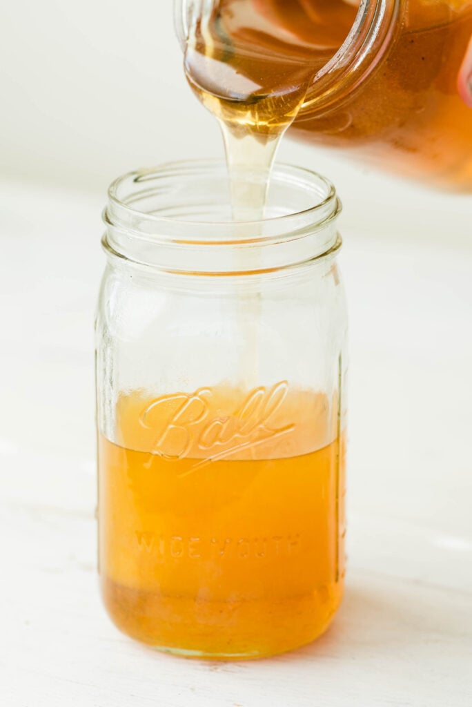 Honey pouring in to a glass jar with strained pumpkin flavored water to make a syrup.